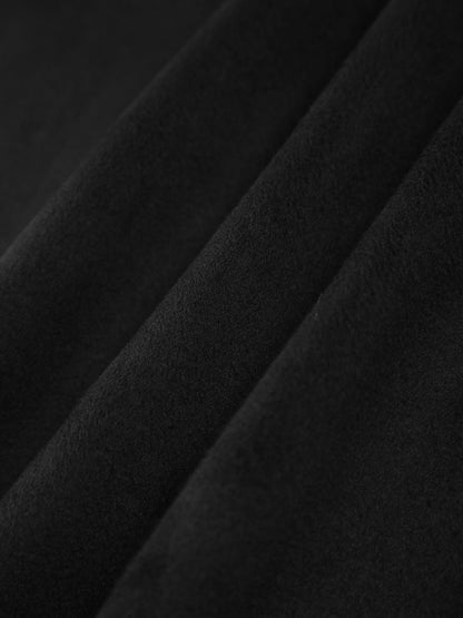 Model sitzt im schwarzen Cape-Mantel mit Schal und Taschen-Details

