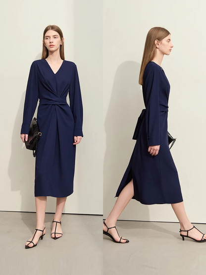 Different angles of a stylish woman wearing a navy blue, long sleeved, midi dress with a ruching and tie design to cinch the waist,  and a slit at the back for ease of movement. The dress looks lose and comfortable. 