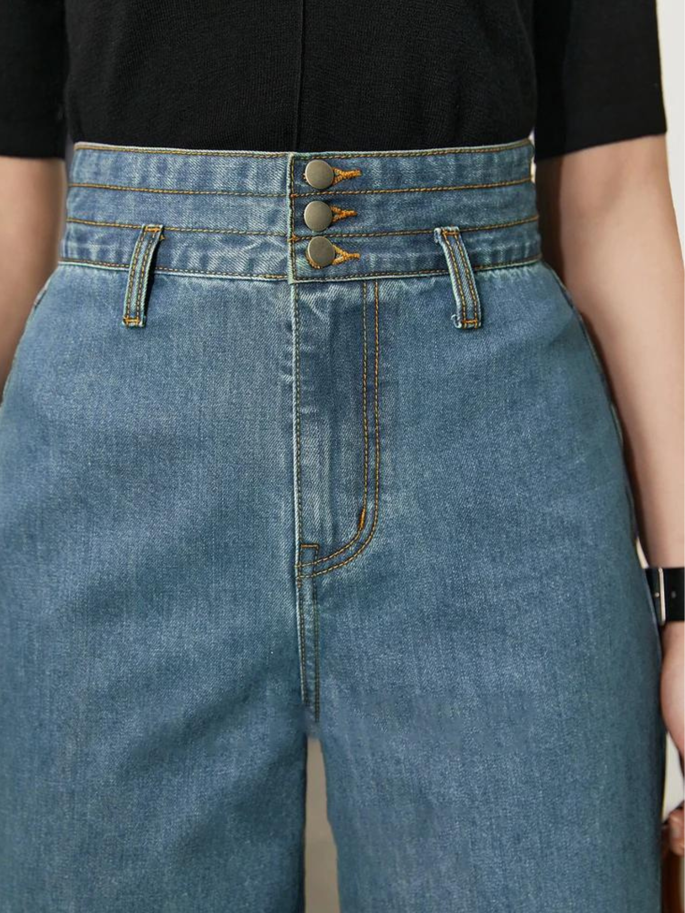 A close up of the waist detailing of a pair of jeans showcasing the three layer button enclosure and cinched waist design.
