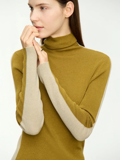 A woman wearing a mock neck, dual toned sweater in light yellow and mustard.