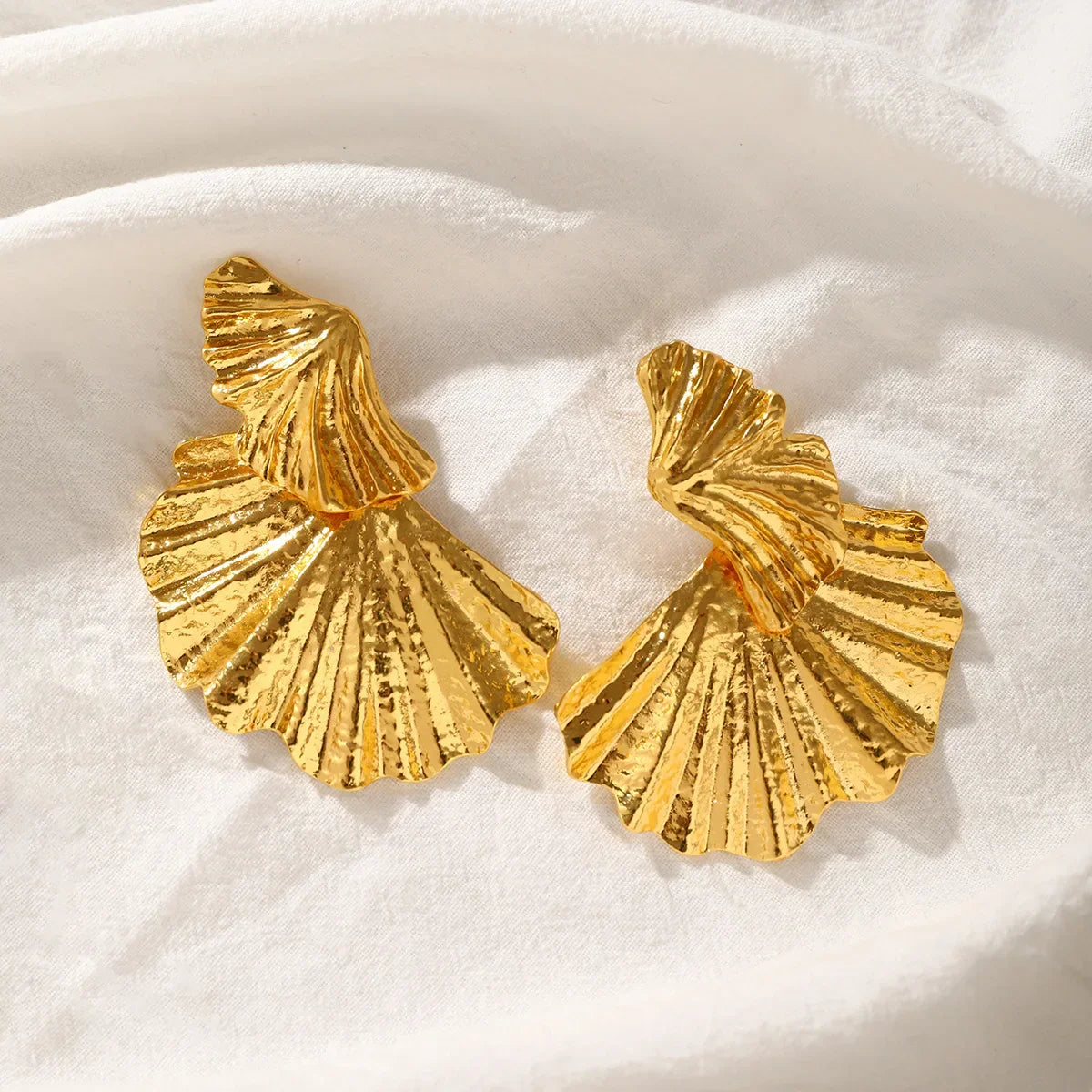 Goldene Statement-Ohrringe mit Muschelform auf Stoff
